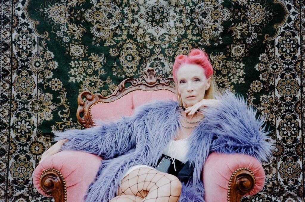 free spirit woman with dyed red hair and a purple fur jacket on vintage red chair