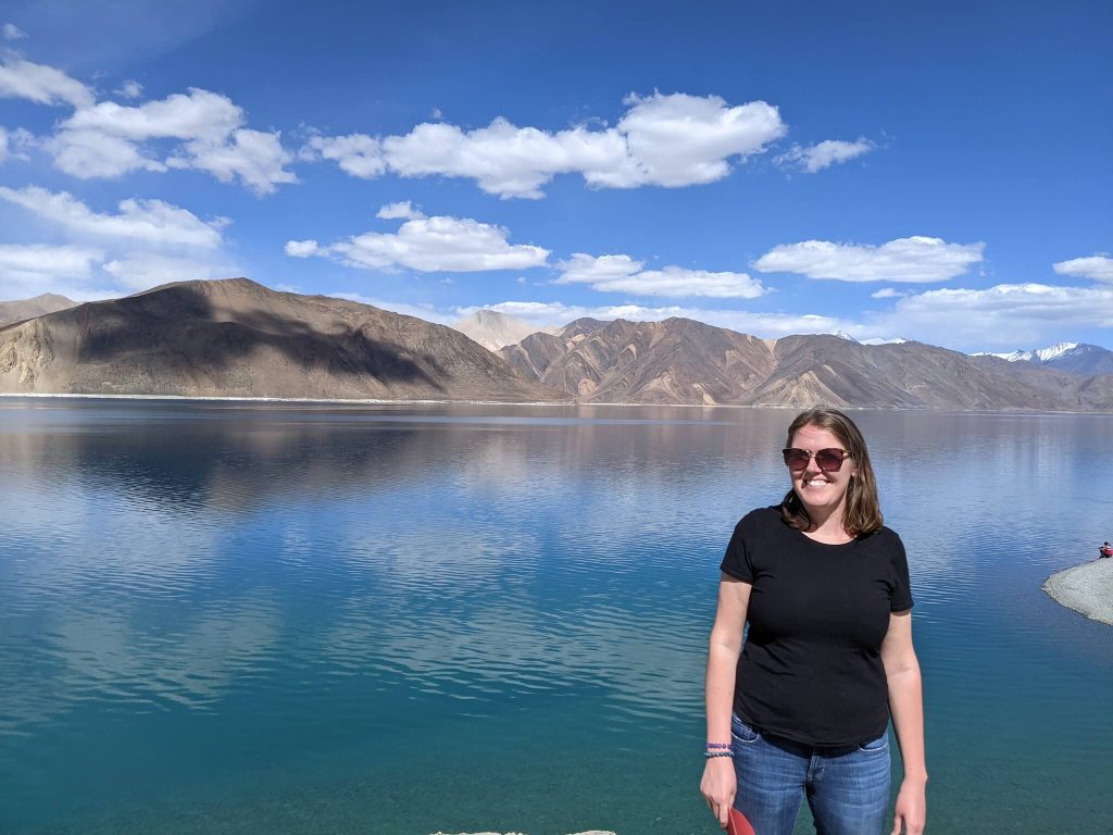 kayla dhankhar standing in front of a beautiful lake in the Himalayas