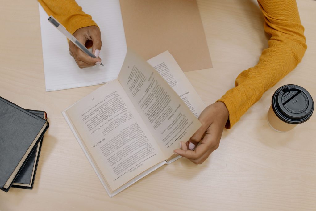 womans hands turning book pages and writing on notepad because The Happiness Trap may require lots of paper to work through