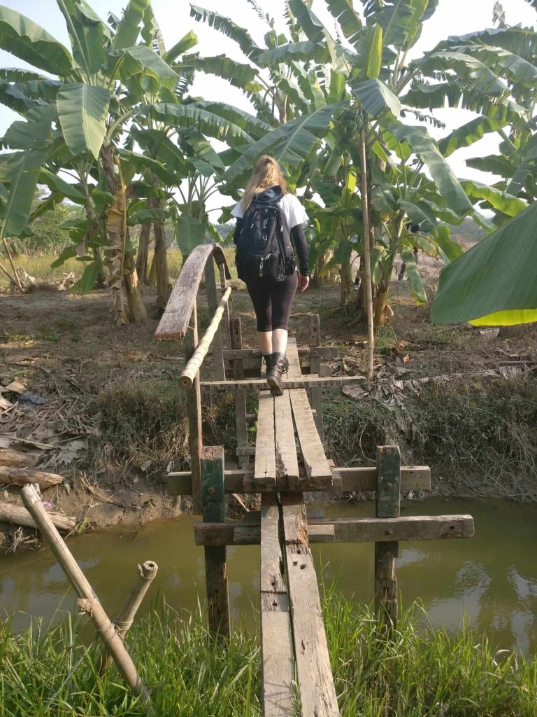 a woman walking on a narrow plank bridge in Myanmar