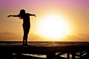 silhouette of a woman feeling freedom with a sunset and beach in the background
